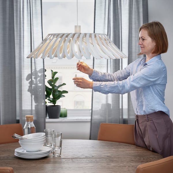 Woman adjusts YTLÄGE lamp, changing shade from closed to open. Alternatively, for a more concise version: adjusting YTLÄGE lamp shade.