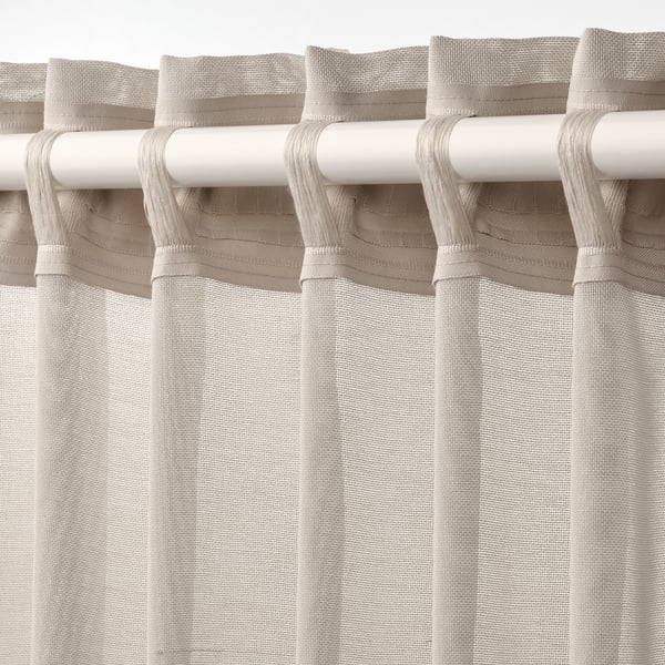 Tringle blanche avec rideaux transparents beiges suspendus, affichant des onglets de fronçage et laissant passer la lumière.