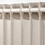 Tringle blanche avec rideaux transparents beiges suspendus, affichant des onglets de fronçage et laissant passer la lumière.