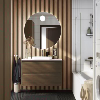 Salle de bain moderne avec meuble-lavabo ÄNGSJÖN en bois foncé, miroir rond, comptoir blanc et accents noirs.