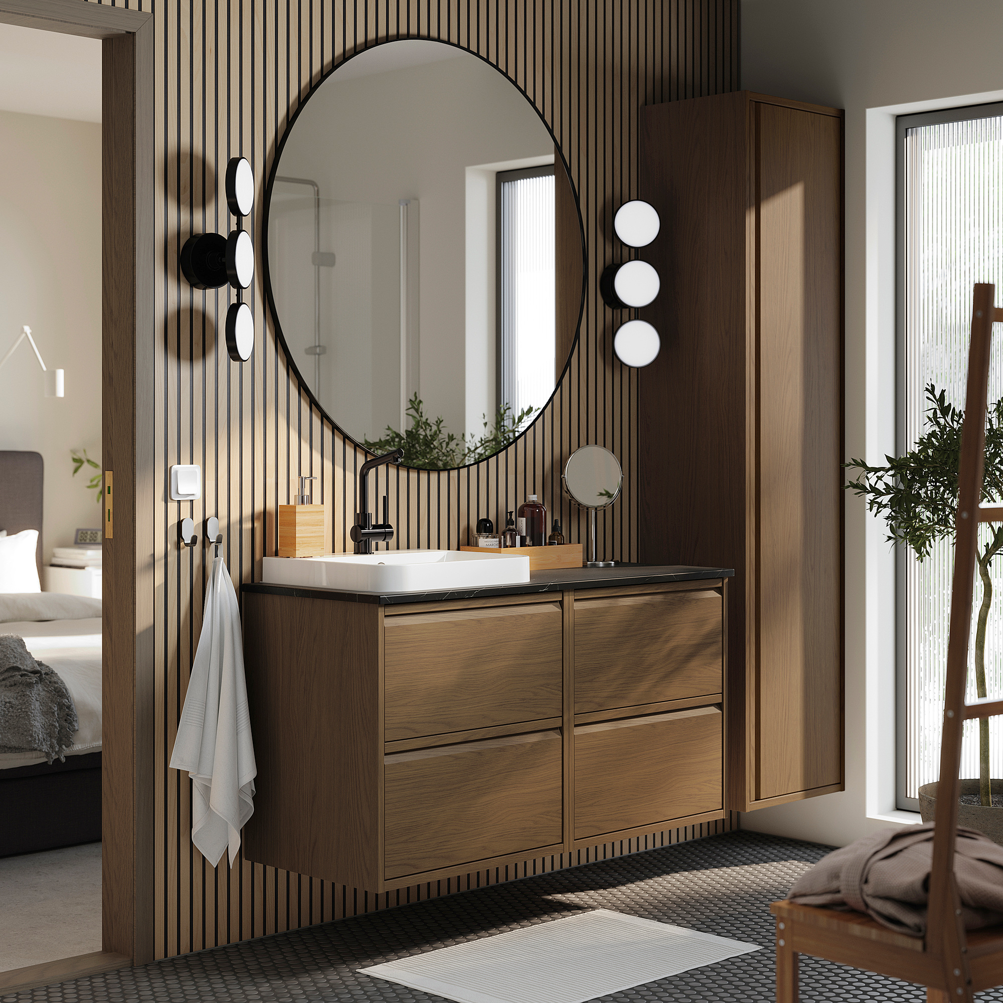 Salle de bain moderne : miroir rond, vanité en chêne, vasque en marbre, murale, plante, serviettes, panier, sol à motifs, lit au-delà.