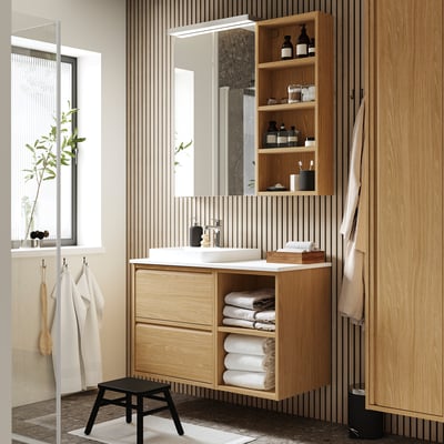 Salle de bain moderne avec meuble-lavabo en bois ÄNGSJÖN, lavabo en marbre, étagères ouvertes, grand miroir, serviettes et tabouret noir. Bois clair, spacieux, aspect épuré.