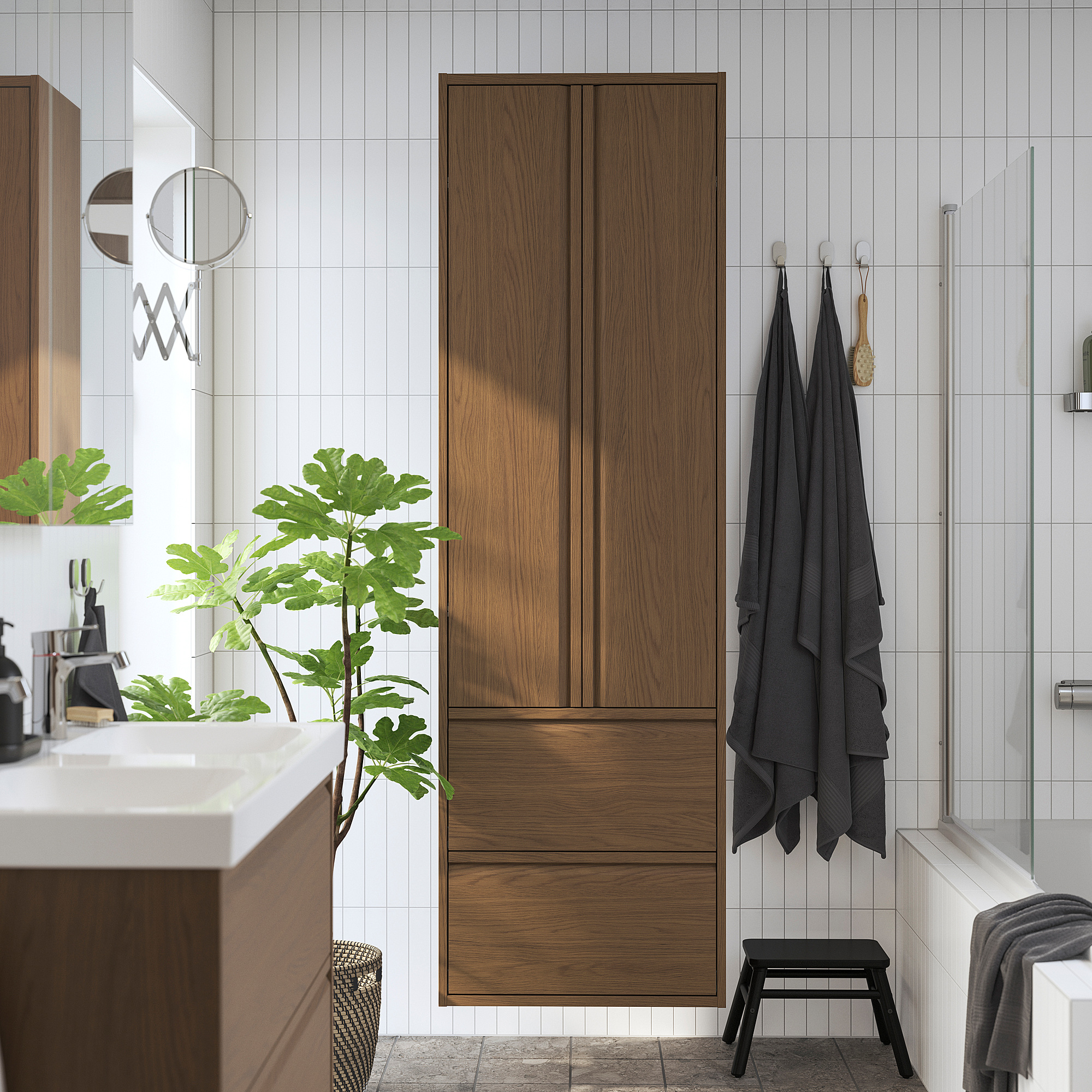 Salle de bain moderne avec grande armoire de rangement en chêne brun, tiroirs et portes. Plantes et serviettes sombres à proximité.