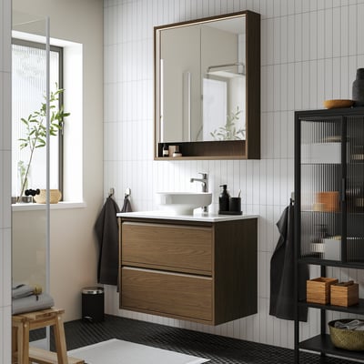 Salle de bain moderne avec meuble en chêne, lavabo blanc et grand miroir. Compact mais fonctionnel, idéal pour les espaces contemporains.