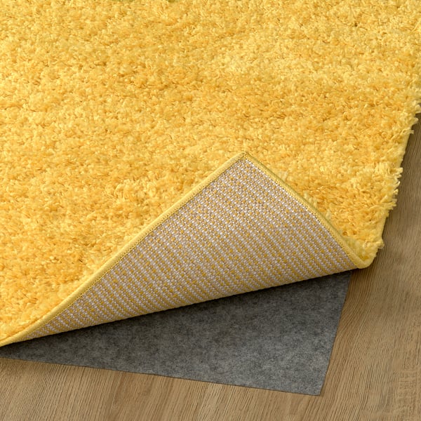 Tapis jaune vif, hirsute avec dos texturé, faisant partie d’une série de tapis conçus pour le confort et l’absorption acoustique.