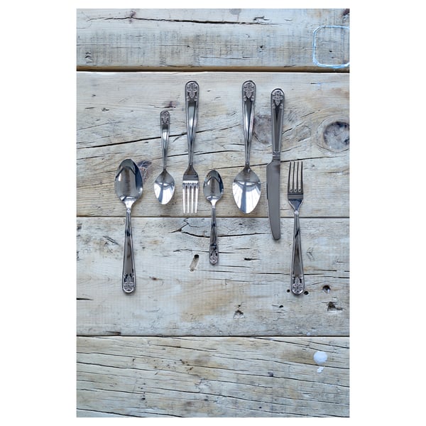 Set de couverts en acier inoxydable : cuillères, fourchettes, couteau, cuillère à café sur bois patiné.