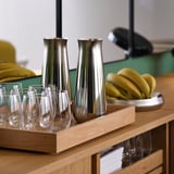 Plateau en bois avec deux carafes en acier brillant et plusieurs verres transparents, prêt à servir des boissons fraîches.