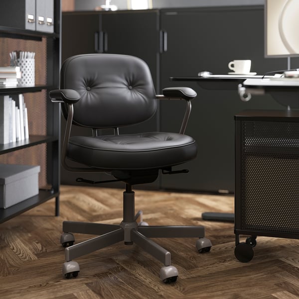 Chaise de bureau en cuir noir avec dossier, roues et accoudoirs réglables dans une pièce en bois.