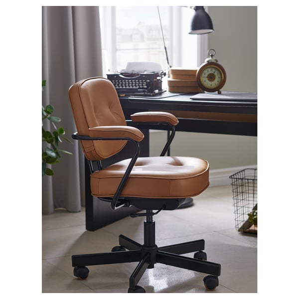 Chaise de bureau en cuir marron avec accoudoirs et roulettes près d’un bureau avec une machine à écrire et des livres.