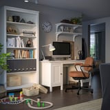 Configuration du bureau à domicile : bureau blanc, chaise en cuir marron, étagères avec des livres, des jouets et une horloge.