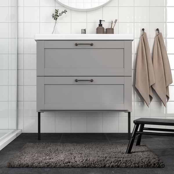 Salle de bain moderne avec tapis gris ALMTJÄRN, meuble-lavabo élégant et serviettes suspendues.