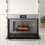 Four à micro-ondes intégré avec une plaque croustillante à l’intérieur, cuisant des aliments dans une cuisine moderne.