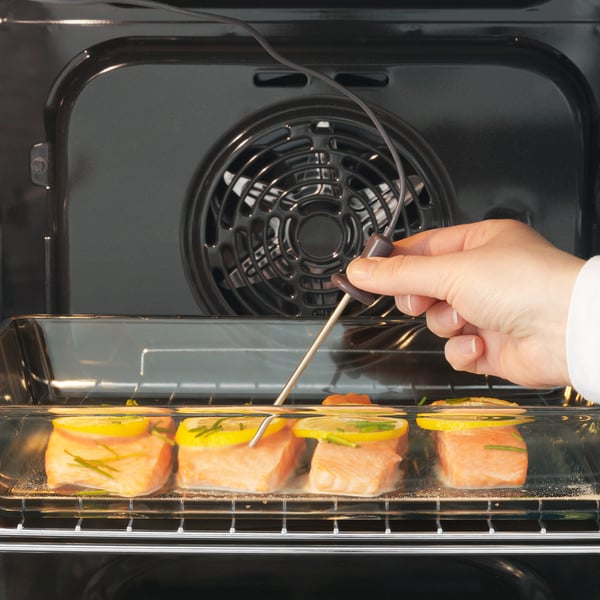 À l’aide de pinces, une main place les filets de saumon garnis de citron dans un four ouvert avec chauffage par convection.