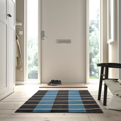 Tapis à carreaux bleu et gris près de la porte, s’étend au tabouret avec sac.