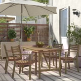 Ensemble de salle à manger d’extérieur en bois d’acacia avec chaises rembourrées et parasol, parfait pour les petits patios. Comprend un bol de fruits, entouré de plantes.