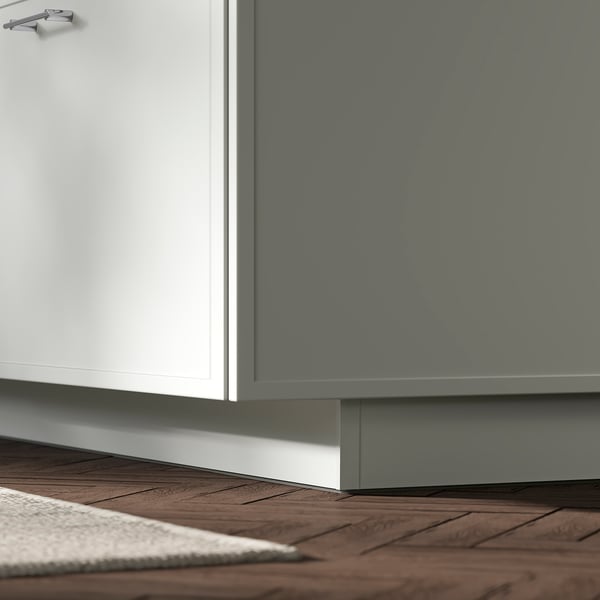 Cuisine moderne avec armoires blanches et grises. Le socle ASPUDDEN blanc comble les lacunes, stylisé sur un plancher en bois.