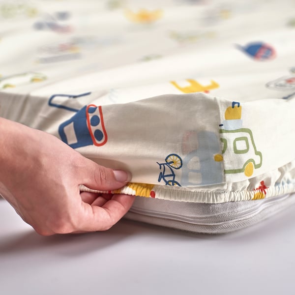 Une main tenant un drap-housse aux motifs colorés de véhicules, adapté à un enfant de 3 ans.