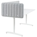 Un bureau BEKANT blanc à hauteur réglable, doté d’une cloison insonorisante grise pour plus d’intimité.