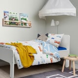 Chambre d’enfant avec literie de véhicule, jeté jaune, livres, baldaquin, lampe, tabouret, tapis, oreiller pour chat.