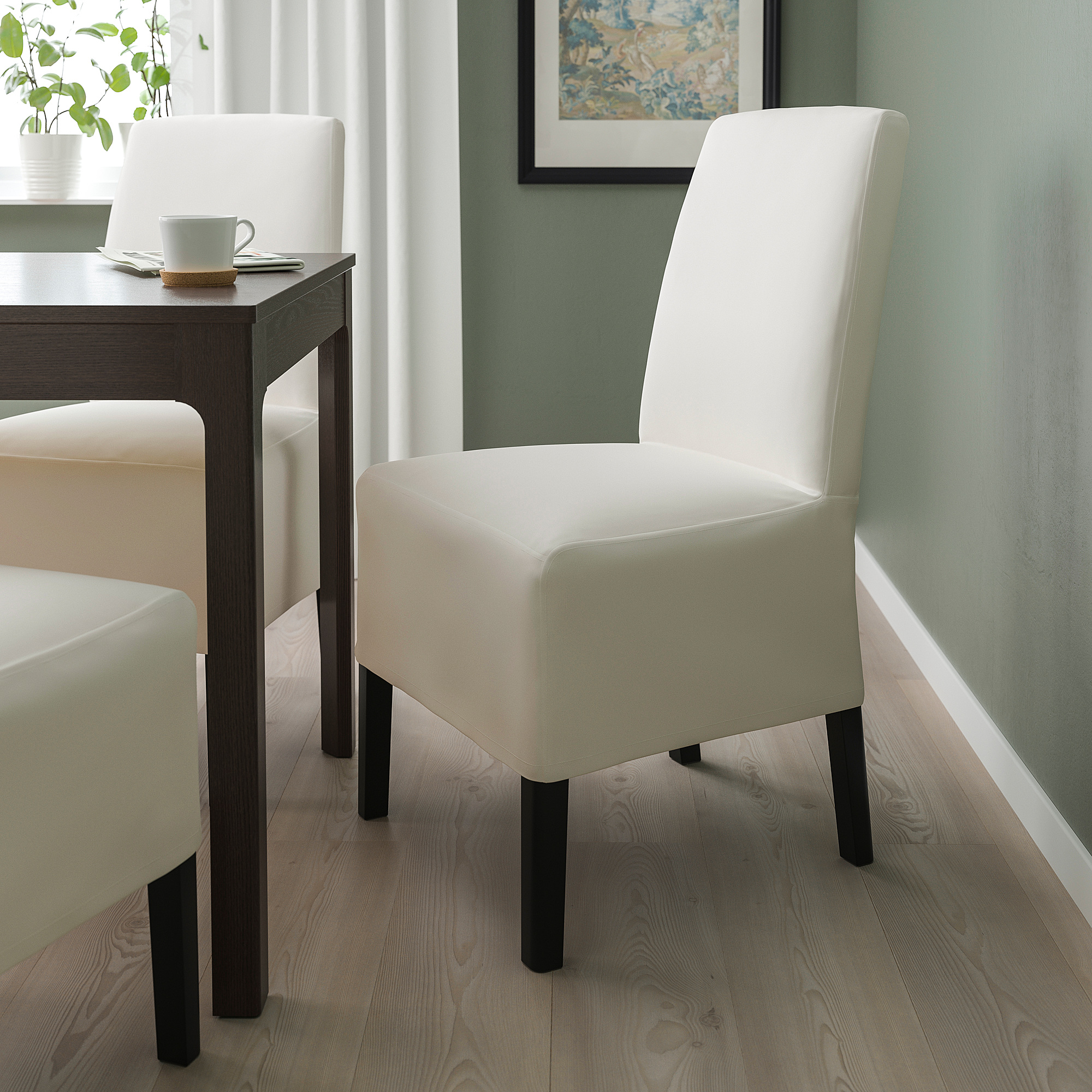 Chaise de salle à manger rembourrée blanche moderne, plus haute que la table, avec des pieds en bois foncé.