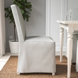 Une chaise rembourrée grise avec un dossier haut et des pieds en bois, adaptée pour s’asseoir confortablement à une table à manger.