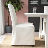 Une chaise moderne avec un dossier haut et un revêtement blanc se trouve près d’une table avec un verre dessus. La chaise est conçue pour le confort et un nettoyage facile.