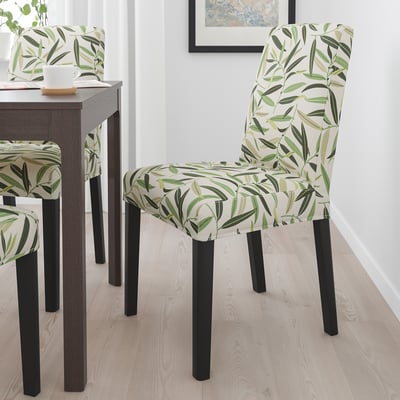 Trois élégantes chaises à motifs verts avec des pieds en bois noir autour d’une petite table à manger.