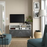 Salon moderne avec banc TV BESTÅ, télévision à écran plat, décoration et chaises bleues. Lampadaire à côté.