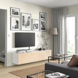Salon moderne avec meuble TV en bois clair, télévision noire, photos encadrées, rideaux gris et canapé noir.