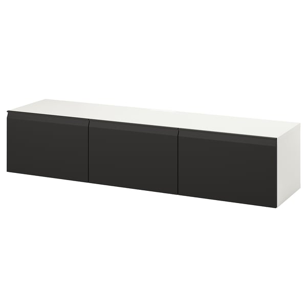 Un banc tv BESTÅ blanc et noir. Il a une forme rectangulaire élégante avec trois compartiments, offrant un design moderne et un grand espace de rangement.