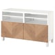 Un banc tv BESTÅ en blanc avec des portes en bois. Il dispose de deux étagères ouvertes et de deux armoires avec charnières à fermeture douce.