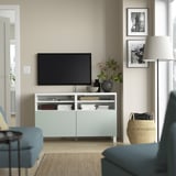 Salon moderne avec banc TV BESTÅ en bleu clair, télévision à écran plat, canapé bleu, panier, lampe et photos en noir et blanc.
