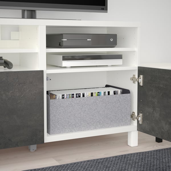Meuble TV BESTÅ blanc avec étagères, console de jeu et boîtiers de jeux.