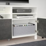 Meuble TV BESTÅ blanc avec étagères, console de jeu et boîtiers de jeux.
