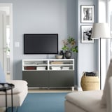 Salon moderne avec banc TV BESTÅ en blanc et noir, doté d’une télévision à écran plat, d’objets décoratifs et d’un tapis bleu.
