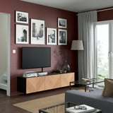 Salon moderne avec des murs bordeaux, grande télévision sur l’unité BESTÅ, bois et noir.