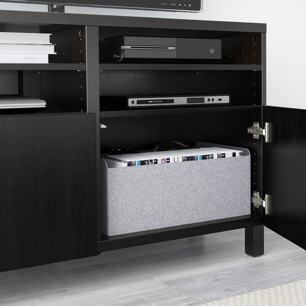 Meuble TV BESTÅ noir, les portes ouvertes révèlent des appareils électroniques et des rangements organisés.