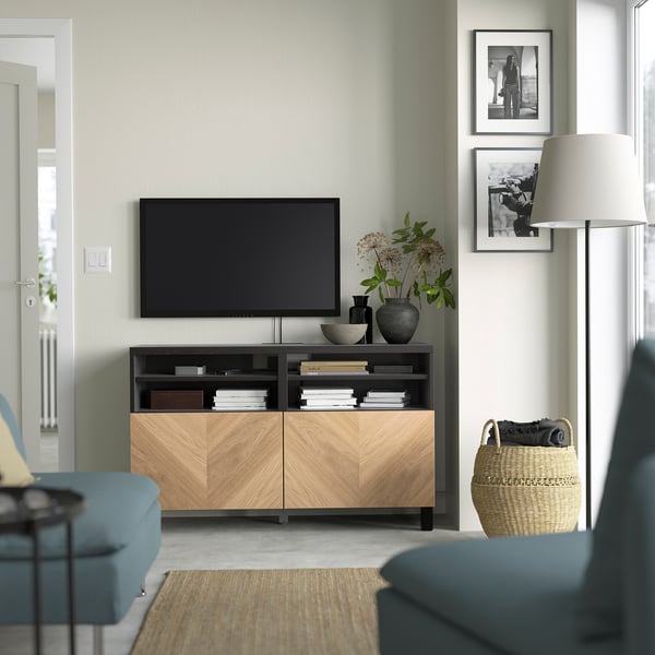 Salon moderne avec banc de télévision BESTÅ, télévision, livres, vases et œuvres d’art. Canapés bleus, lampadaire et panier à proximité.