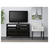 Configuration moderne du salon : meuble TV noir avec rangement, télévision à écran plat, chaise blanche et œuvres d’art de la tour Eiffel.