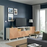 Salon moderne avec banc TV BESTÅ en bois clair, mur sombre, canapé gris, grande télévision à écran plat et objets de décoration.