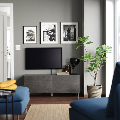 Salon moderne avec banc TV BESTÅ gris, télévision à écran plat noir, chaises bleues et trois photos encadrées au-dessus.
