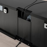 Banc TV noir avec gestion des câbles, pieds réglables et tiroirs ouvre-poussoirs. Les câbles sont soigneusement organisés à travers des ouvertures de câble arrière.