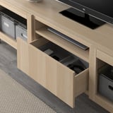 Meuble tv en bois clair avec tiroir ouvert affichant les articles stockés. Conçu pour la gestion et l’organisation des câbles.