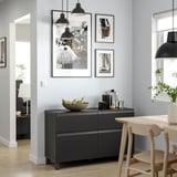 Salle à manger moderne avec buffet BESTÅ noir, suspensions et chaises en bois. Le mur présente des œuvres d’art encadrées.