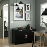 Salon moderne avec buffet BESTÅ, lampes, art, bol, pichets, chaise. Mur d’accent vert.