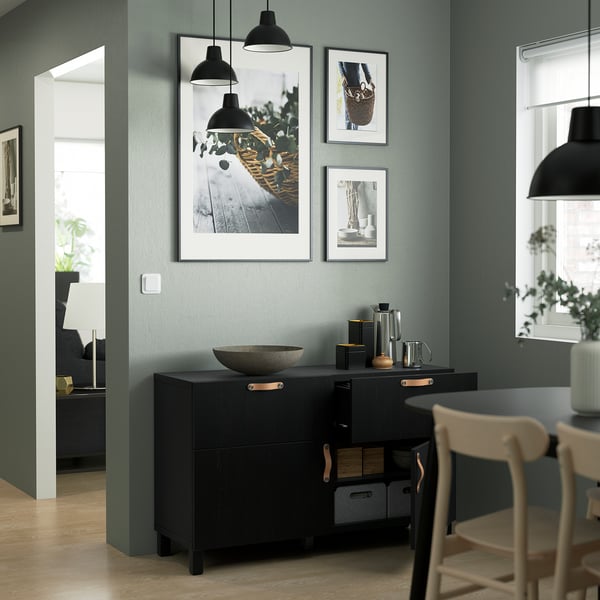 Cuisine moderne un buffet BESTÅ avec des étagères réglables, des tiroirs à fermeture douce et de nombreux rangements. Au-dessus, trois photos encadrées sont accrochées à un mur végétal.