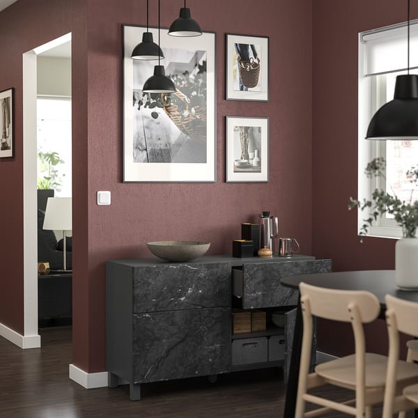 Espace de vie moderne avec des murs rouges profonds, avec des œuvres d’art encadrées en noir et blanc, un buffet en marbre et des chaises en bois.