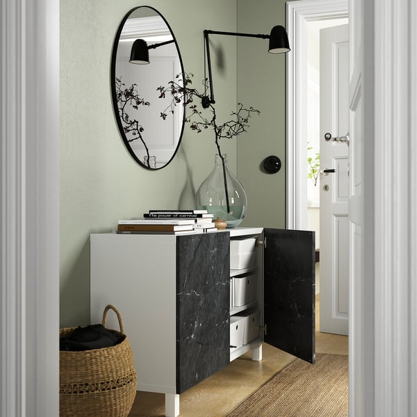 Chambre moderne avec armoire de rangement ouverte, exposant des livres et un vase, à côté d’un panier tressé et d’un miroir mural.