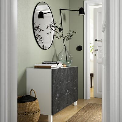 Couloir moderne avec buffet BESTÅ noir et blanc, miroir et décor. Panier à côté. Porte d’entrée vers une pièce lumineuse.