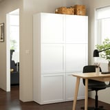 Unité de rangement BESTÅ blanche dans l’espace de vie, plus haute que le bureau adjacent, avec des paniers tressés sur le dessus.
